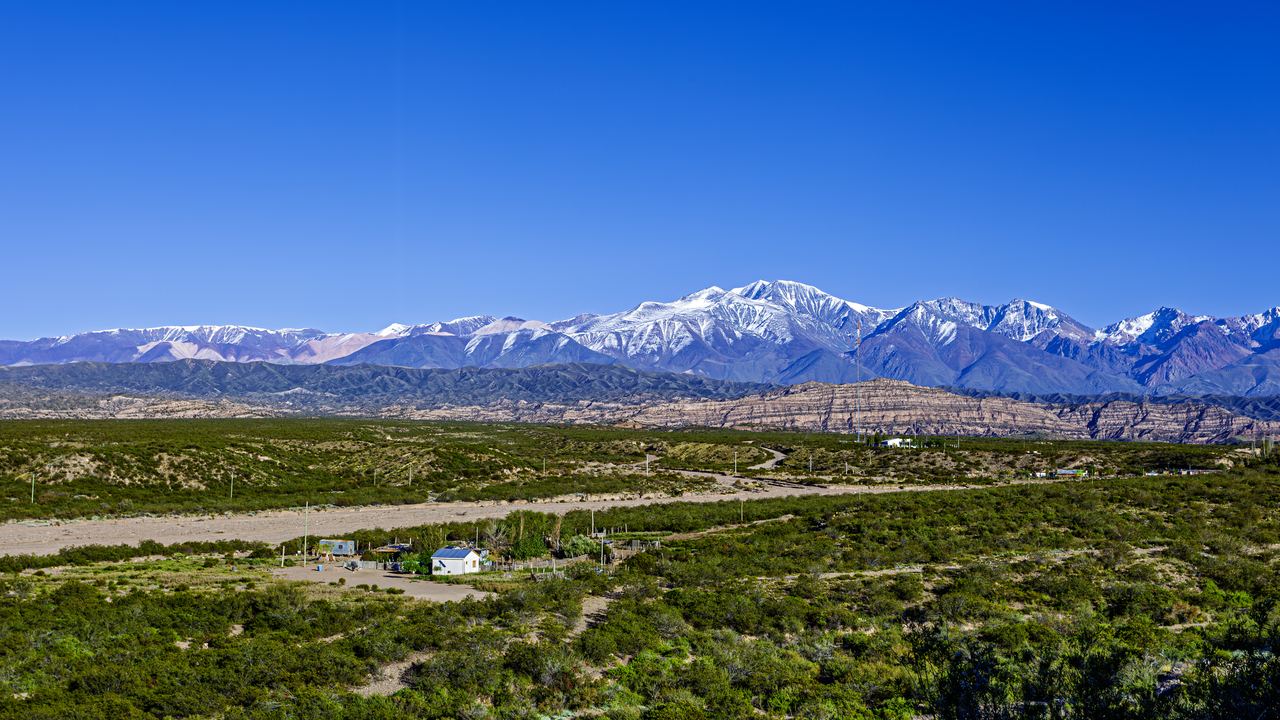 Snow-dusted Andes rising above green scrubland and a farmhouse in Mendoza province