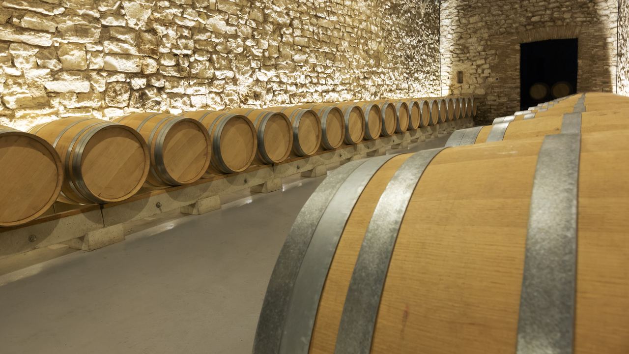 Oak barrels lined along a stone wall in a wine cellar in La Rioja