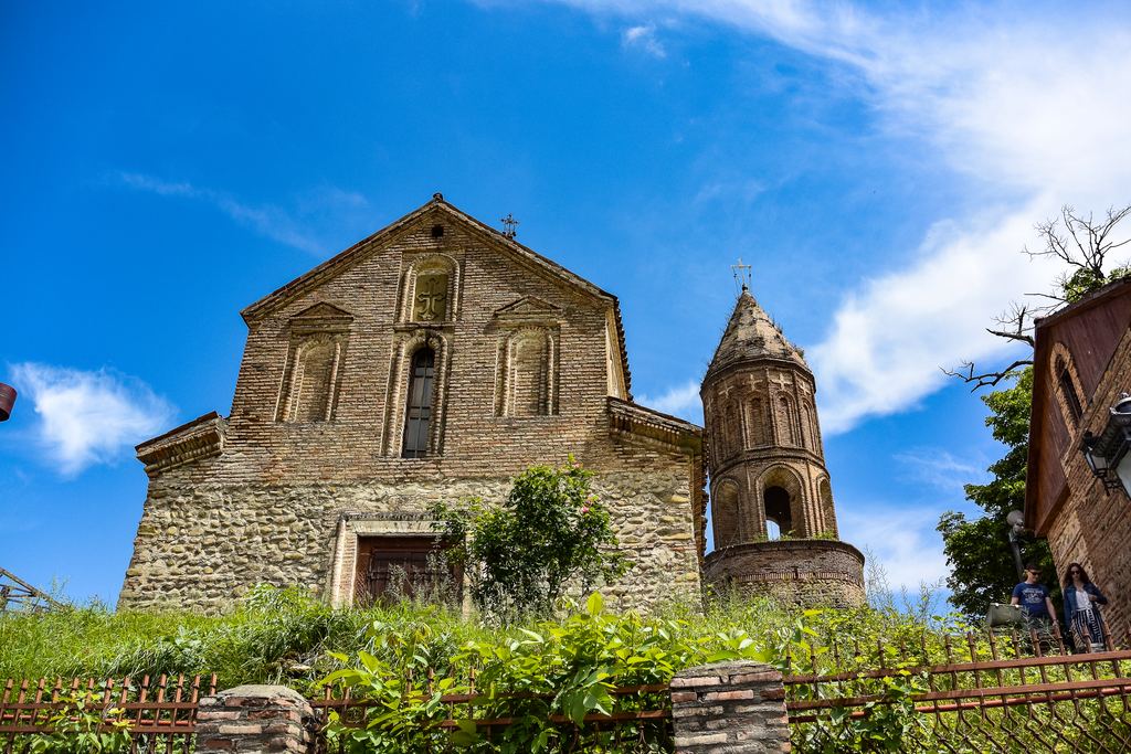 Brick church with a round bell tower beside a stone wall in Georgia under a blue sky