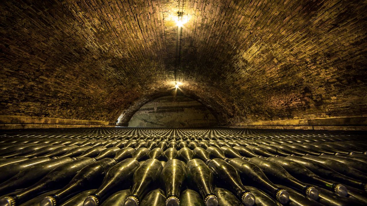 Bottles of sparkling wine lying in rows under a brick-vaulted cellar ceiling