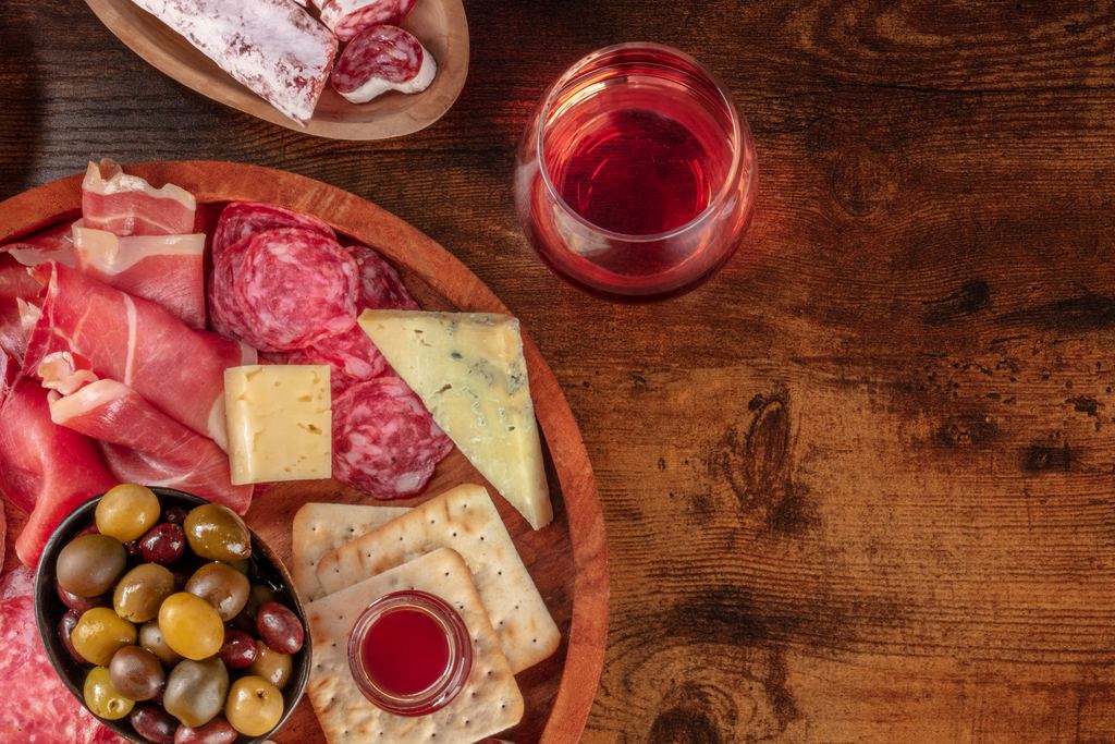 Wooden board of cured meats, cheese, olives and crackers beside glasses of wine