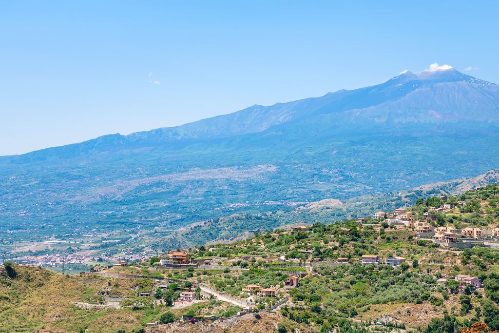 Mount Etna with a plume above the summit and villages on the green slopes below