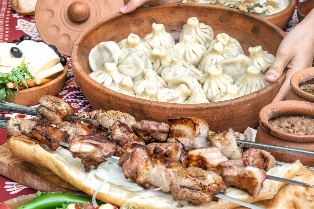 Table laid with dumplings, grilled skewers, bread and salad in clay bowls on a patterned cloth