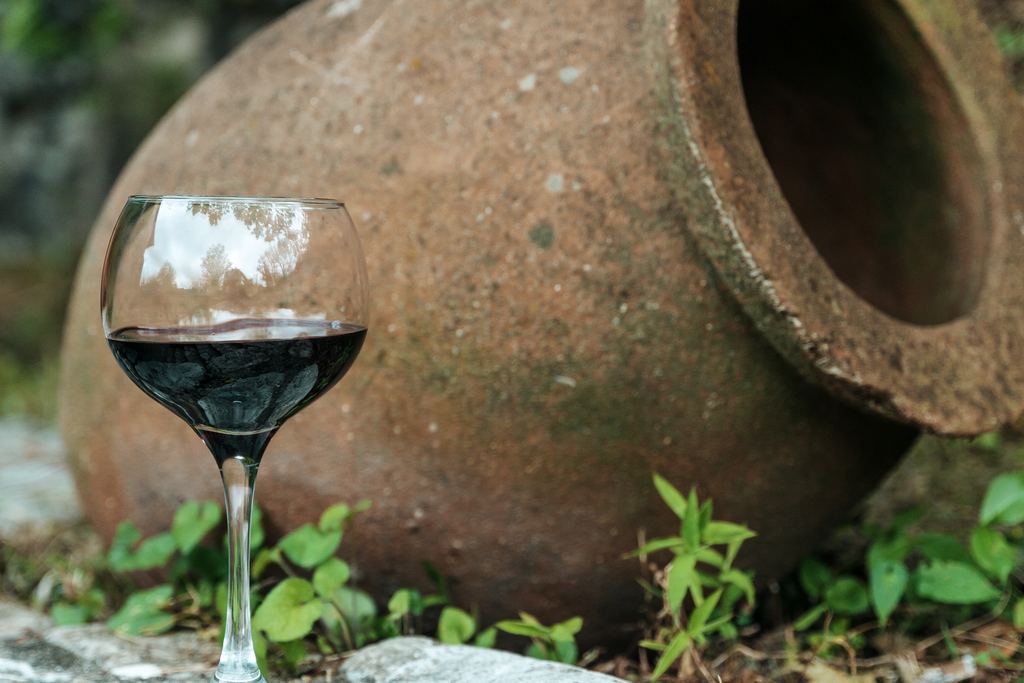 Glass of red wine standing beside a large clay jar, the vessel type used for qvevri wine