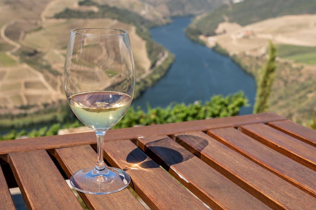 Glass of white wine on a wooden terrace table with terraced vineyard hillsides and a river valley behind