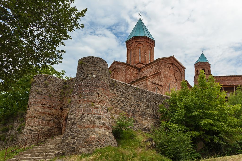 Round brick tower and stone walls of the royal fortress of Gremi in Kakheti with the church behind