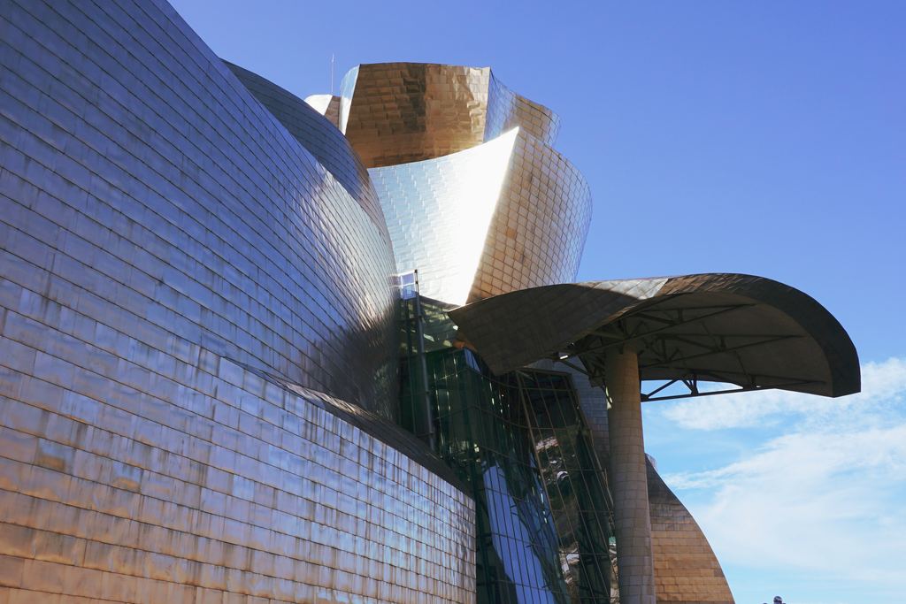Titanium-clad curves of the Guggenheim Museum in Bilbao beside the water under a blue sky