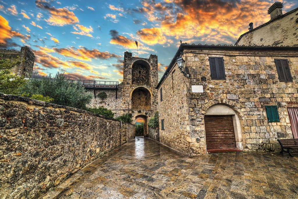 Stone gate and medieval walls of Monteriggioni under a sunset sky