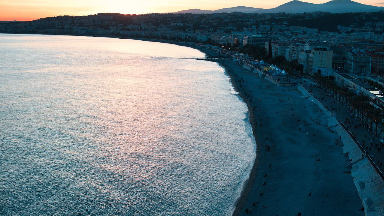 Curving coastline and pebble beach of Nice at sunset, with hills behind