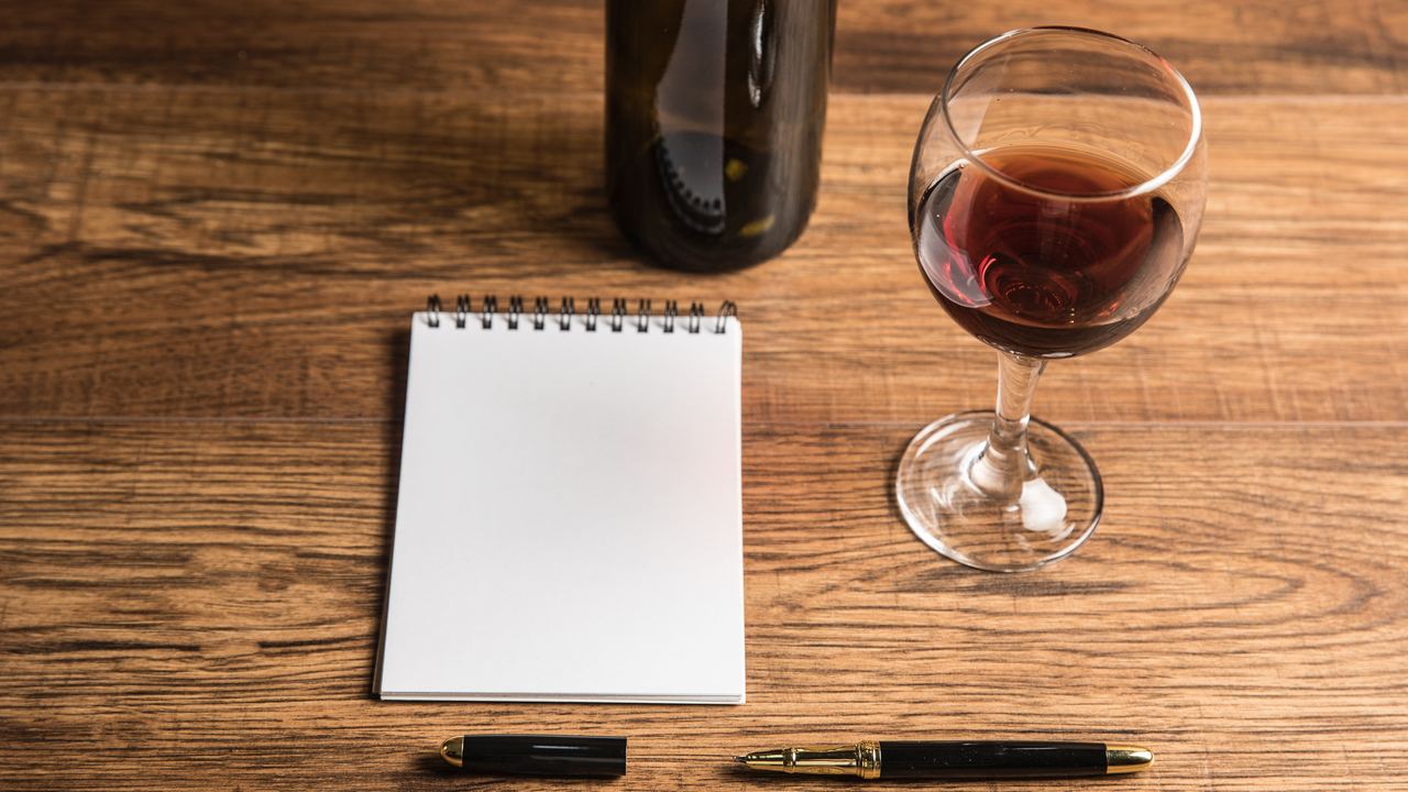 Blank notepad and pen beside a glass of red wine and a bottle on a wooden table, for planning a wine trip