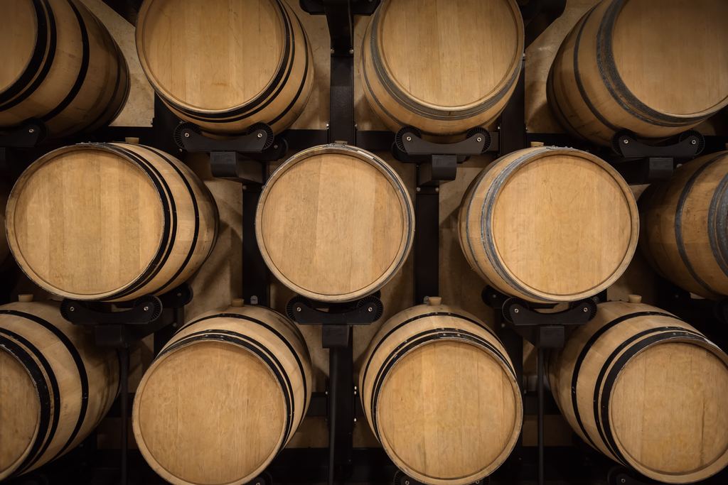 Rows of oak wine barrels stacked on iron racks in a winery cellar
