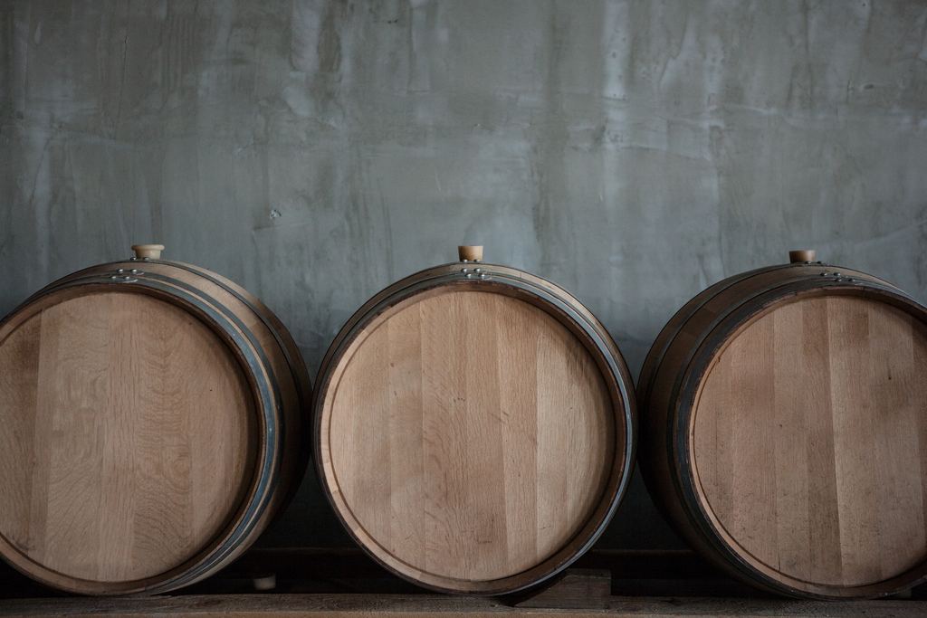 Three oak wine barrels stacked against a concrete wall in a cellar