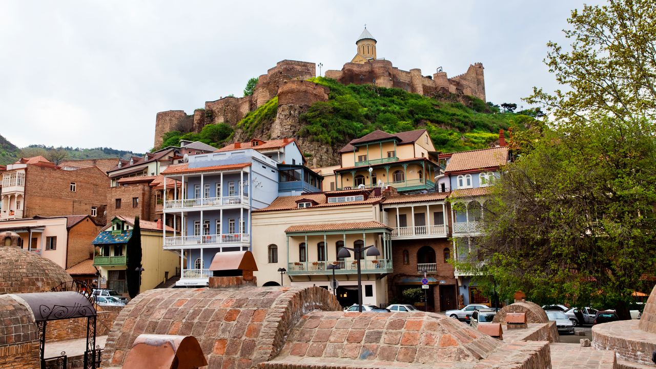 Old Tbilisi houses with wooden balconies below a fortress on the hill