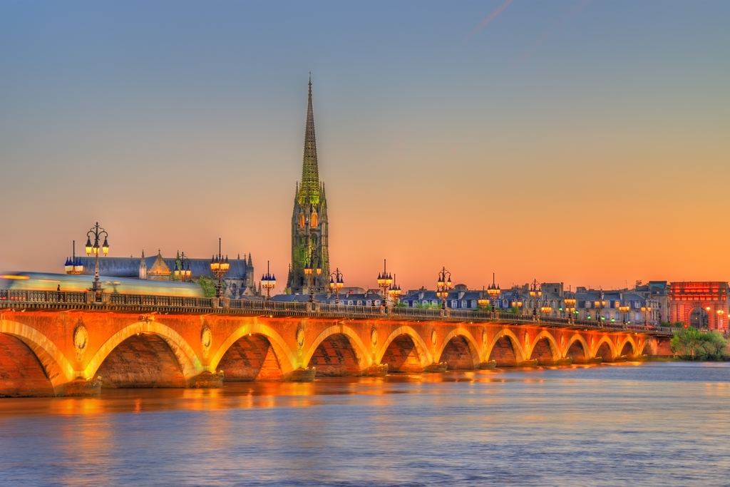 The Pont de Pierre lit at dusk with the spire of the Saint-Michel basilica, Bordeaux