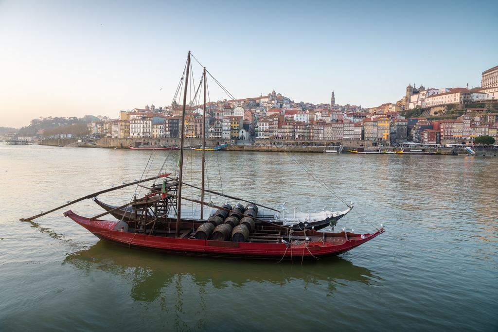 A traditional rabelo boat loaded with port wine barrels on the Douro river, with the Porto riverfront behind