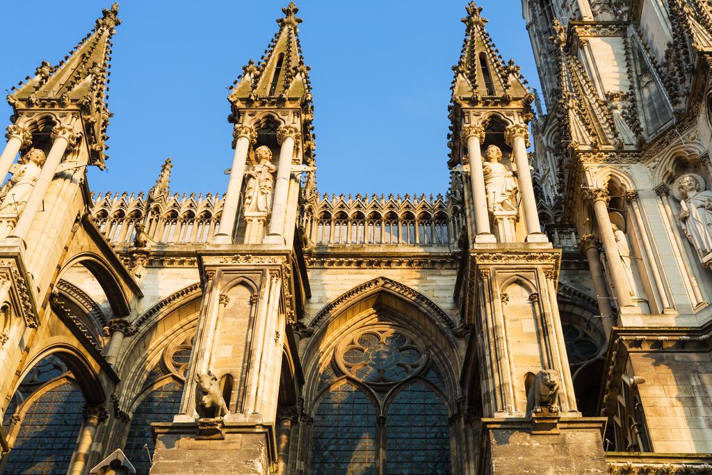 Gothic pinnacles, statues and tall stained-glass windows on the side of Notre-Dame de Reims cathedral in warm evening light, Reims, Champagne, France