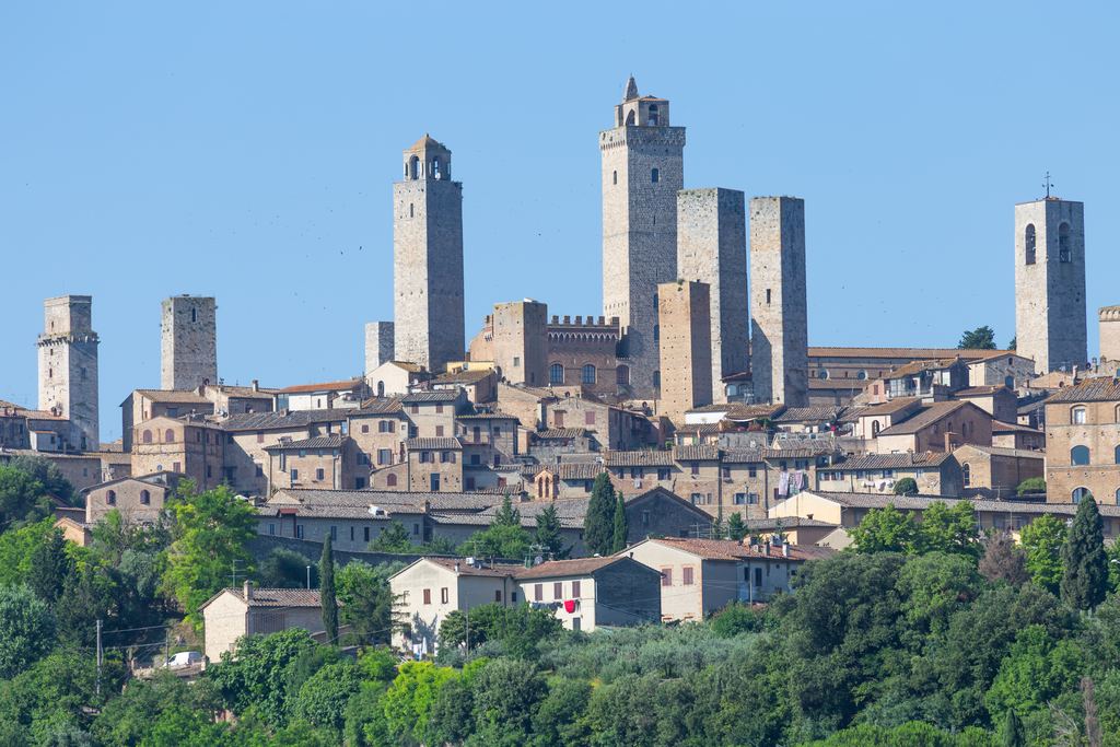 The medieval towers of San Gimignano rising above green Tuscan hills under a clear blue sky