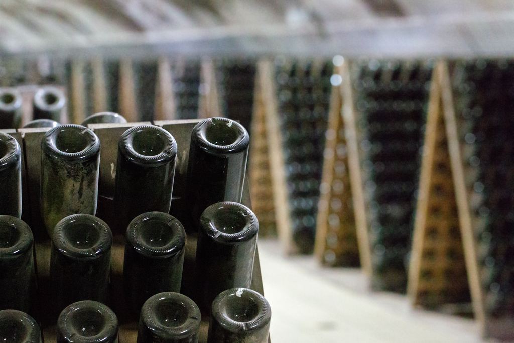 Sparkling wine bottles resting neck down on wooden riddling racks in a cellar