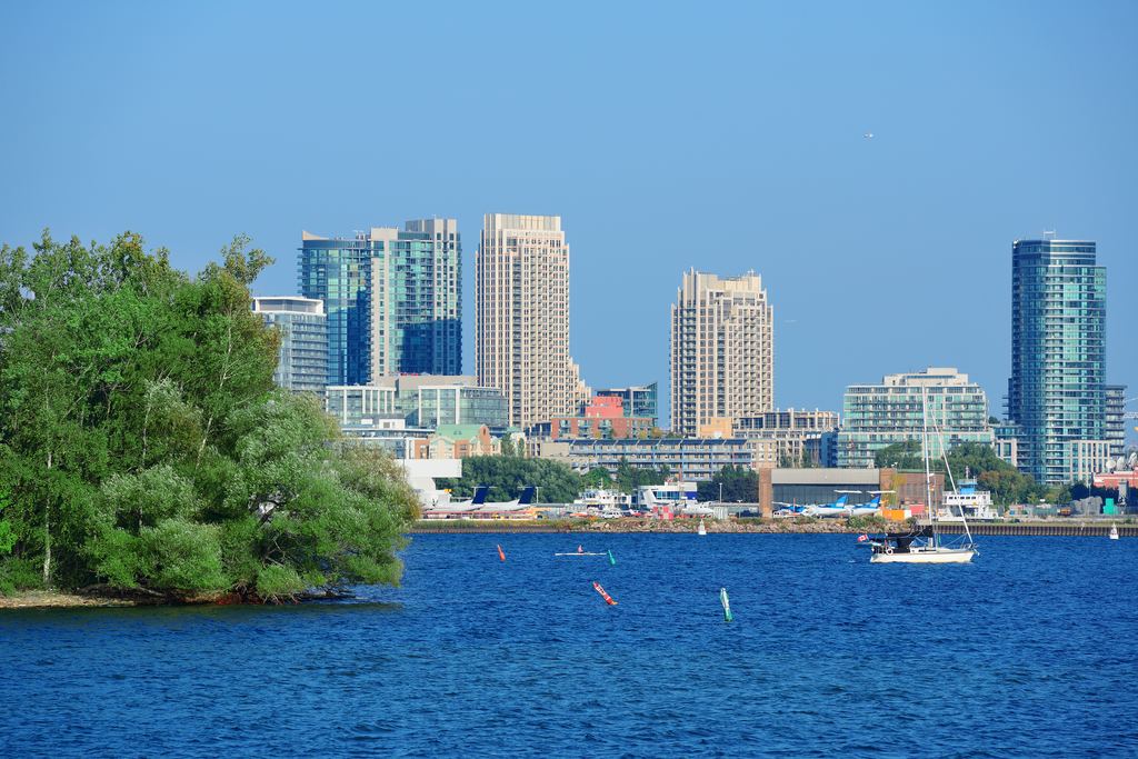 Toronto waterfront towers seen across Lake Ontario with a sailing boat in the foreground