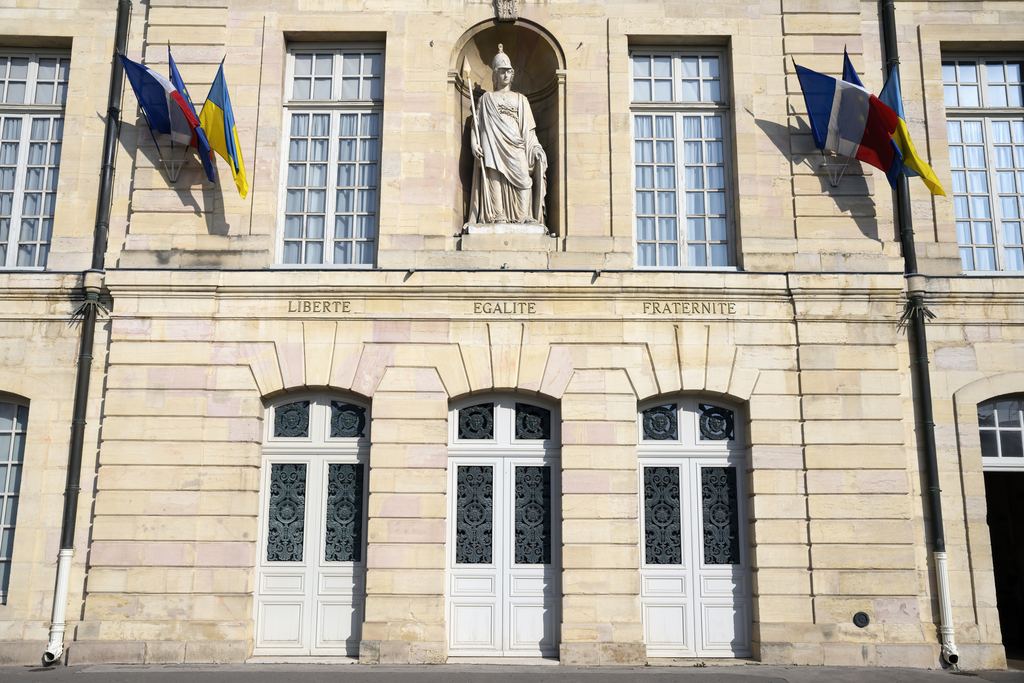 Stone facade of the town hall in Dijon with flags and a statue in a niche