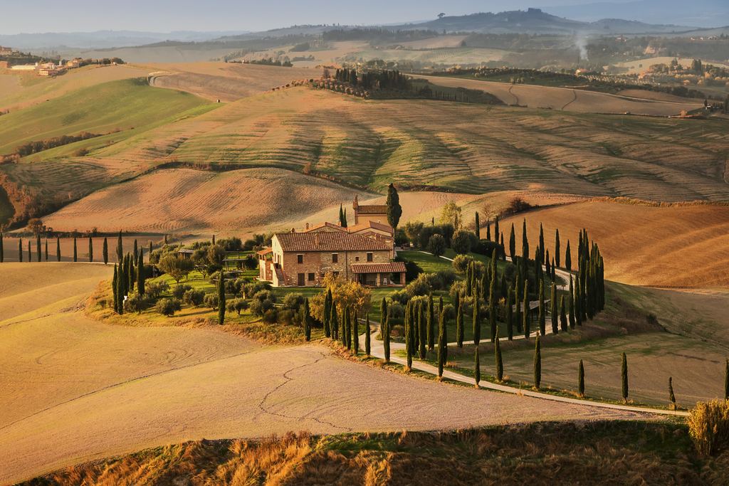 Stone farmhouse ringed by cypress trees on golden rolling hills in the Val d'Orcia, Tuscany, at sunset