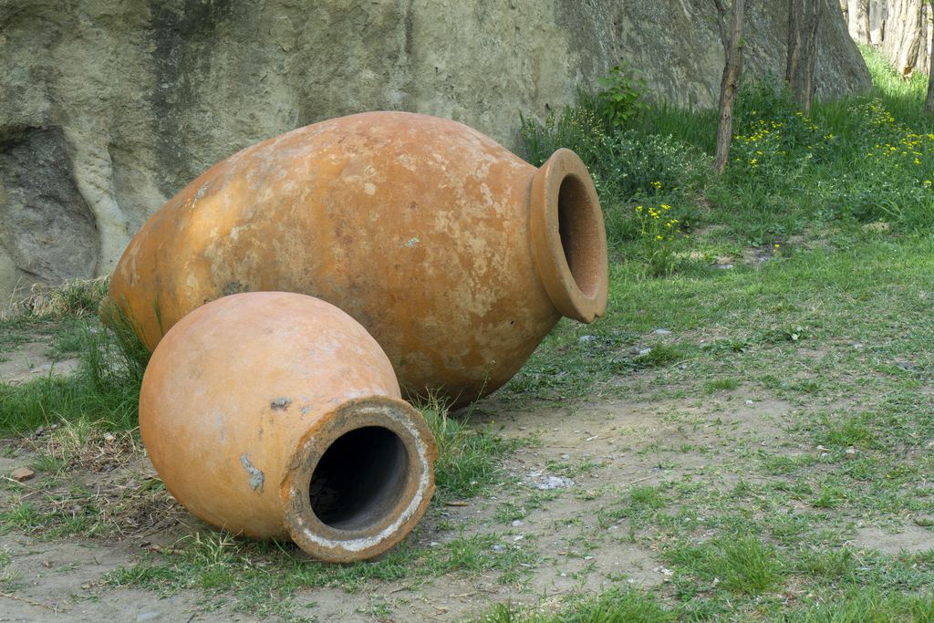 Two earthenware qvevri of different sizes lying on the grass next to a rock, the clay vessels used for fermenting and ageing traditional Georgian wine