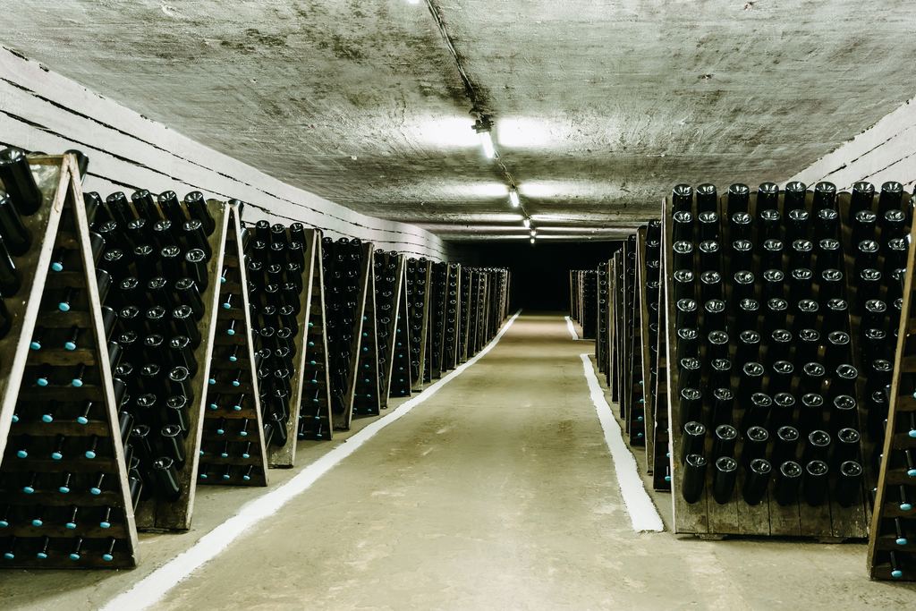 A long underground cellar tunnel lined with racks of sparkling wine bottles ageing neck down
