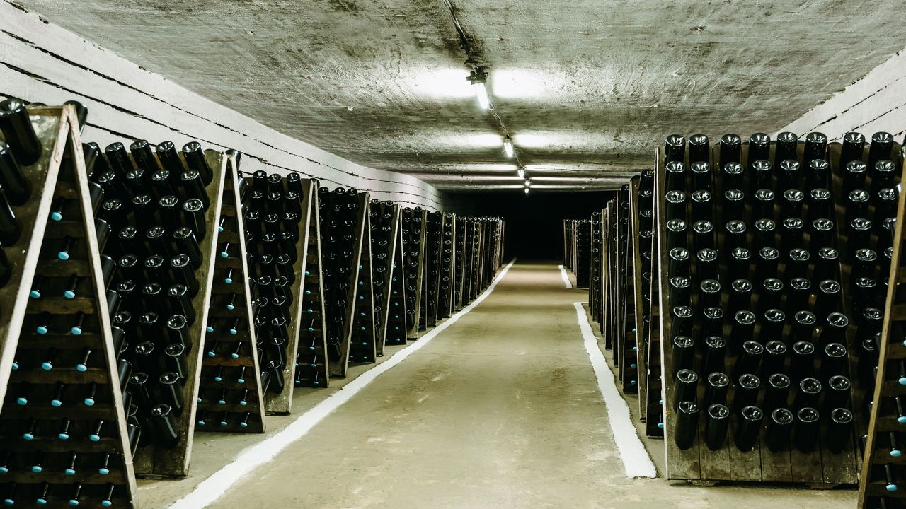 A long underground cellar tunnel lined with racks of sparkling wine bottles ageing neck down