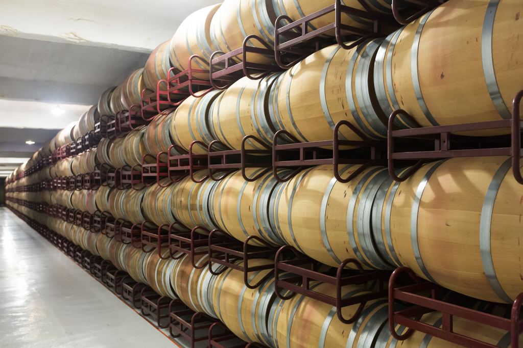 Rows of oak wine barrels stacked on racks in a winery cellar