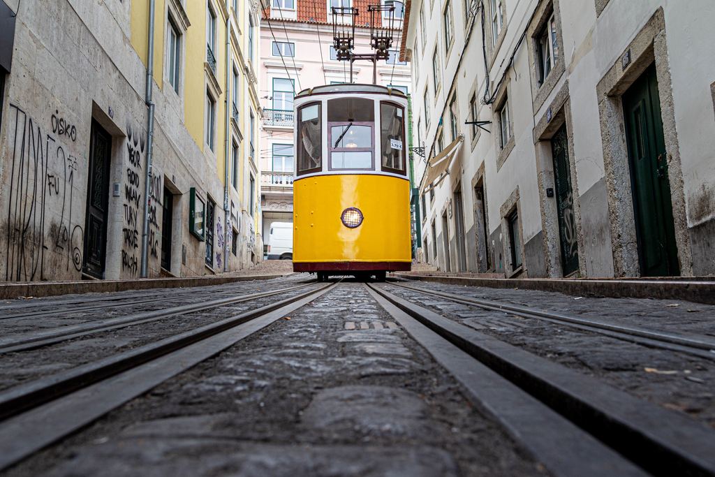 Yellow tram going down a narrow street between old buildings in Lisbon, Portugal